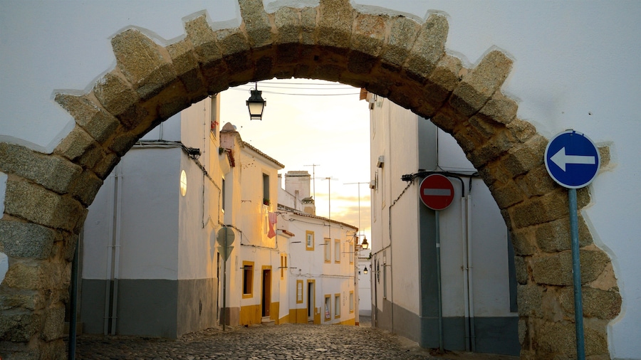 Uma rua de paralelepípedos sob um arco de pedra, com edifícios de ambos os lados.