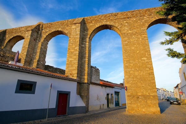 A stone archway with a white building and a red door in the foreground.