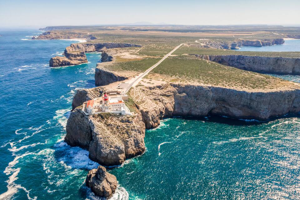 A coastal landscape with a prominent cliff, a lighthouse, and a road leading to a fortified structure.