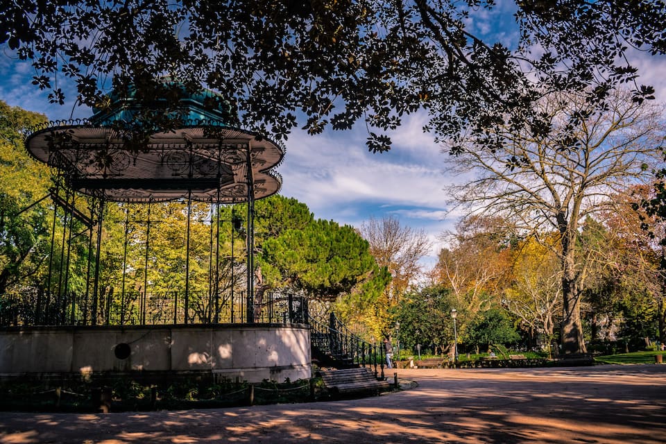 A gazebo in a park with trees and a clear sky.
