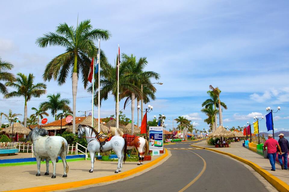 Una calle bordeada de palmeras, una estatua de caballo y banderas coloridas.