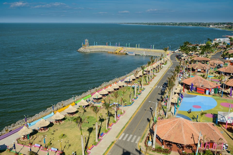 A coastal promenade with thatched-roof structures, a pier, and a colorful playground.