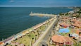 A coastal promenade with thatched-roof structures, a pier, and a colorful playground.