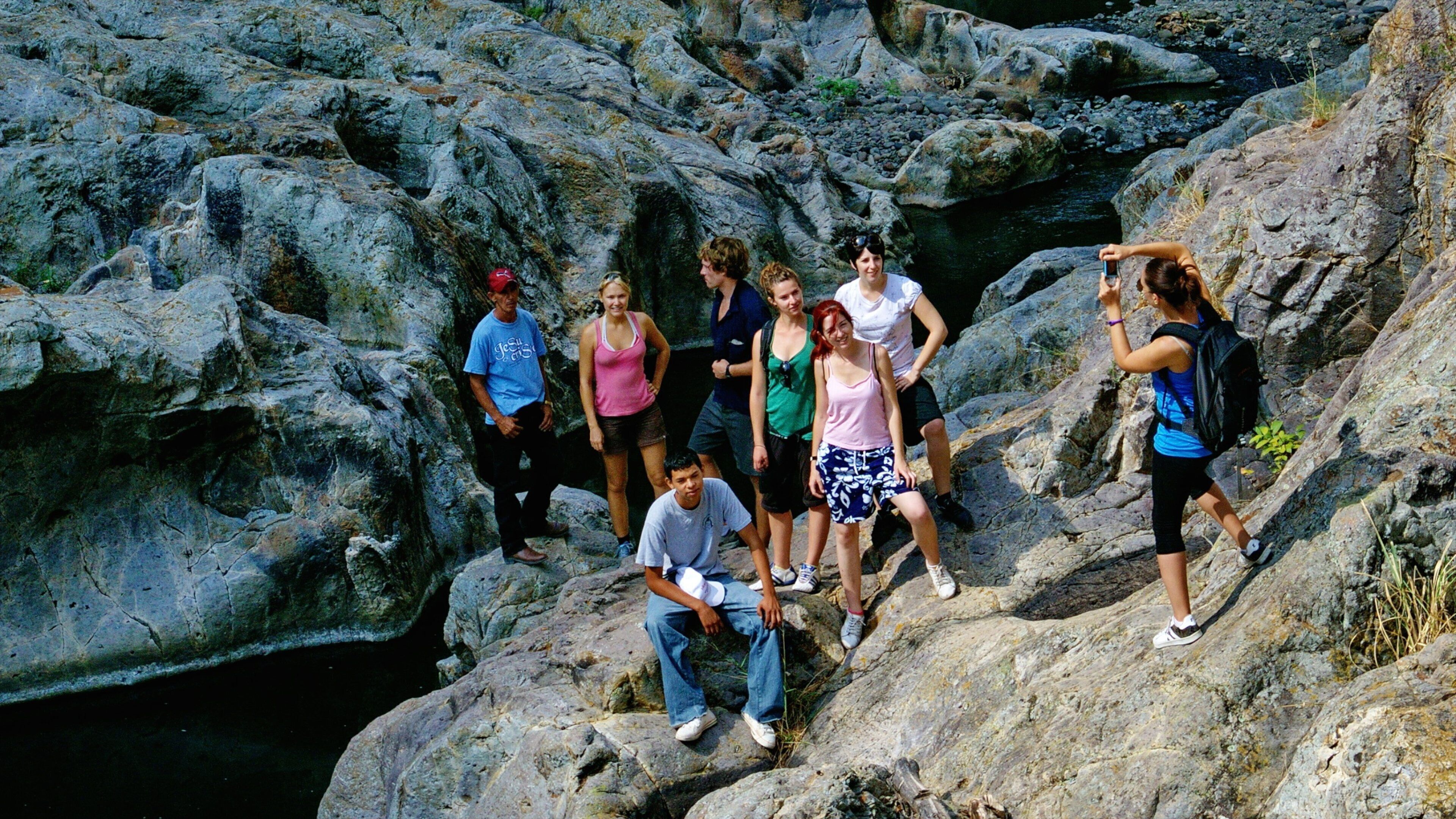 A group of people on rocky terrain with a stream in the background.