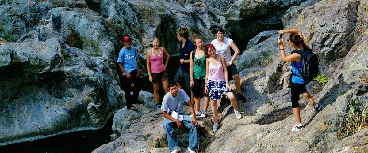 A group of people on rocky terrain with a stream in the background.