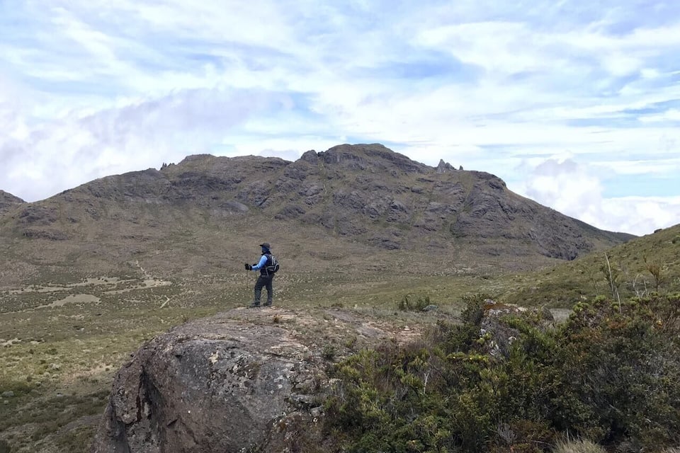 A hiker on a rocky outcrop overlooking a mountainous landscape.