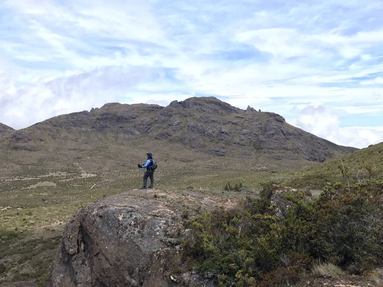 A hiker on a rocky outcrop overlooking a mountainous landscape.