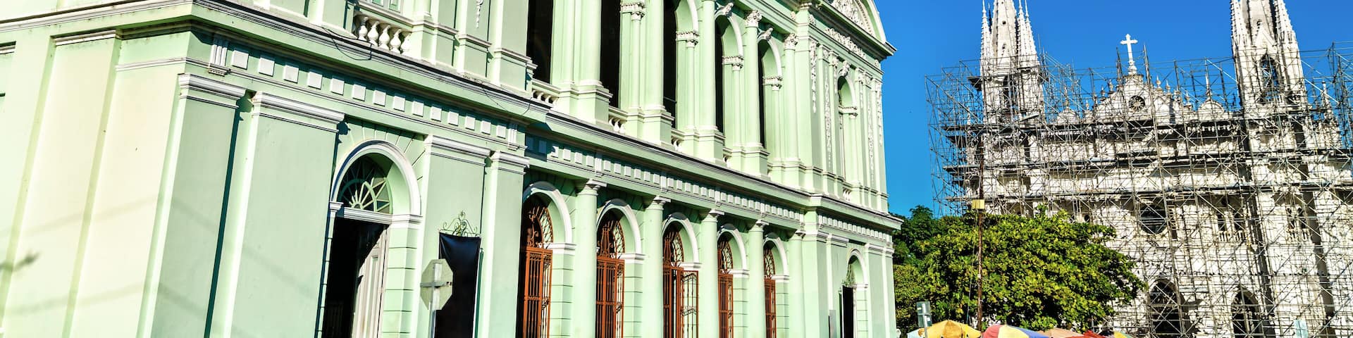 Un edificio verde de estilo clásico con detalles ornamentales y una gran catedral al fondo.