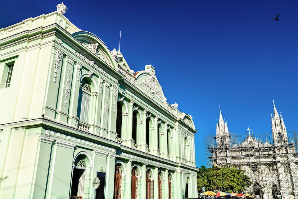 Un edificio verde de estilo clásico con detalles ornamentales y una gran catedral al fondo.