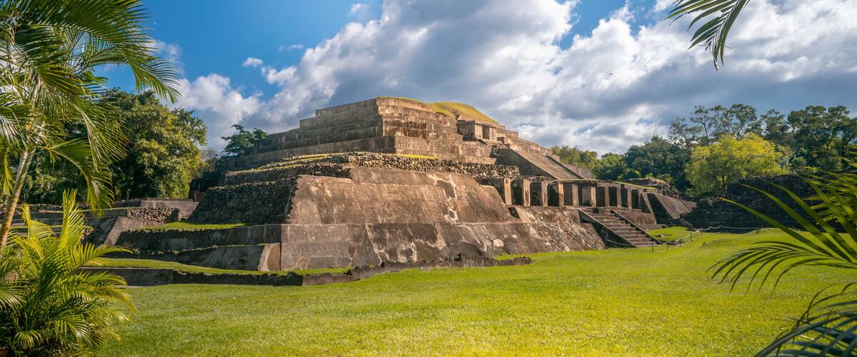 A large ancient pyramid structure surrounded by lush greenery and palm trees.