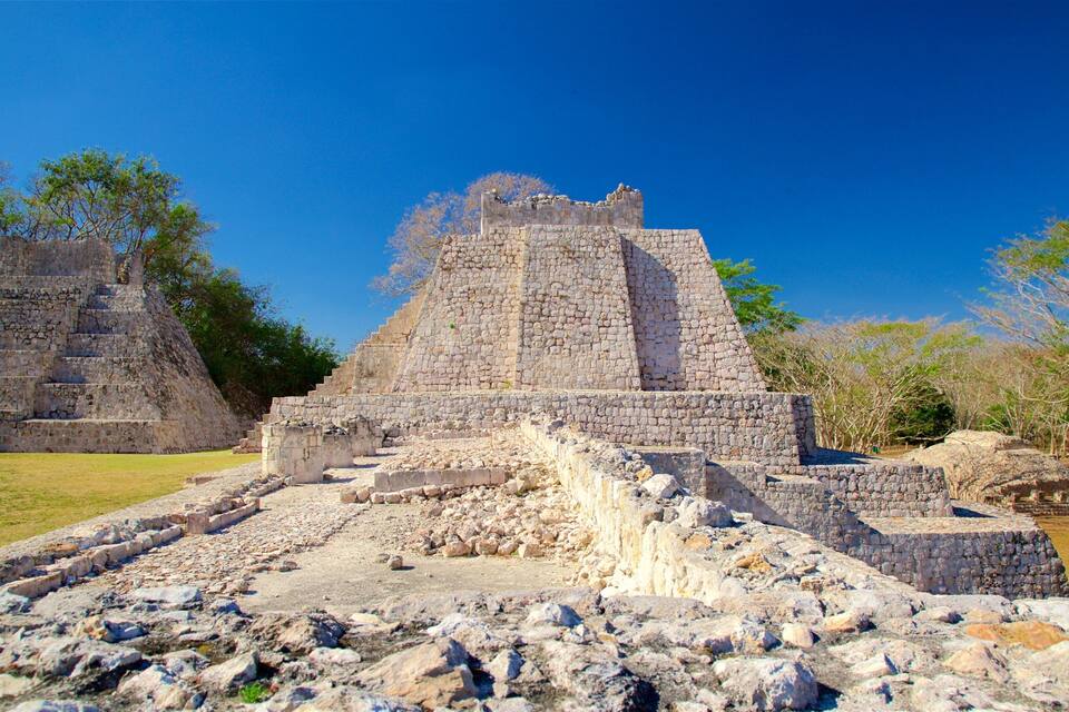 Ancient stone ruins with a large pyramid structure surrounded by trees and grassy areas.