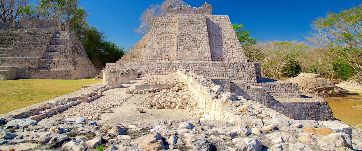 Ancient stone ruins with a large pyramid structure surrounded by trees and grassy areas.