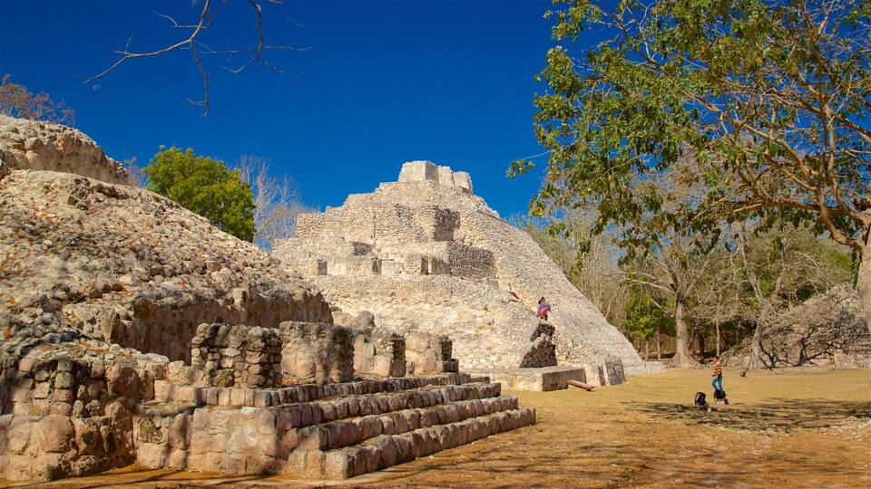 Ancient stone ruins with a pyramid-like structure, a staircase leading up to it, and a person walking nearby.