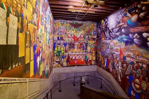 A vibrant mural with historical figures and symbols, a staircase, and a red banner.