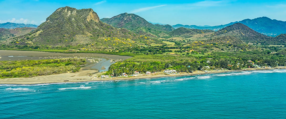 A coastal landscape with mountains, a beach, and a river.