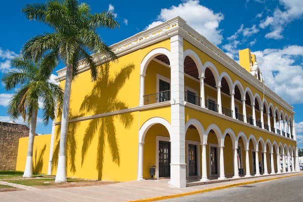 Un bâtiment jaune avec des arches blanches et un palmier.