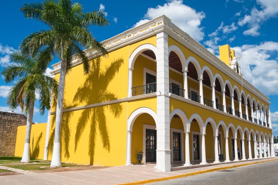 Un edificio amarillo con arcos blancos y una palmera.