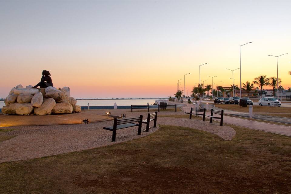 A sculpture of a woman sitting on rocks by the water at sunset.