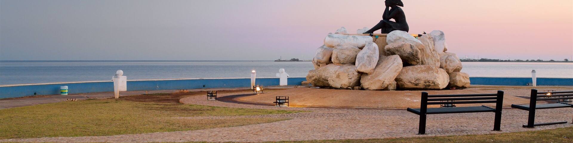 A sculpture of a person sitting on rocks by the sea at sunset.