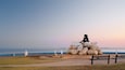 Une sculpture représentant une personne assise sur des rochers, au bord de la mer, au coucher du soleil.