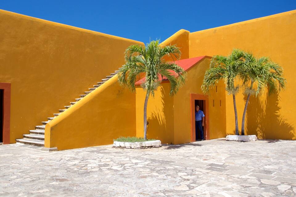 A courtyard with yellow walls, a stone floor, and palm trees.