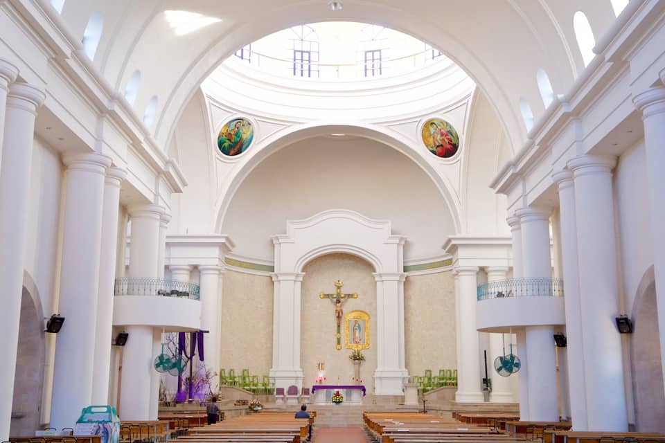 Interior de una iglesia con columnas blancas, un altar central y dos altares laterales.