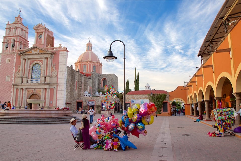 Uma praça com uma igreja rosa, uma fonte e balões coloridos.