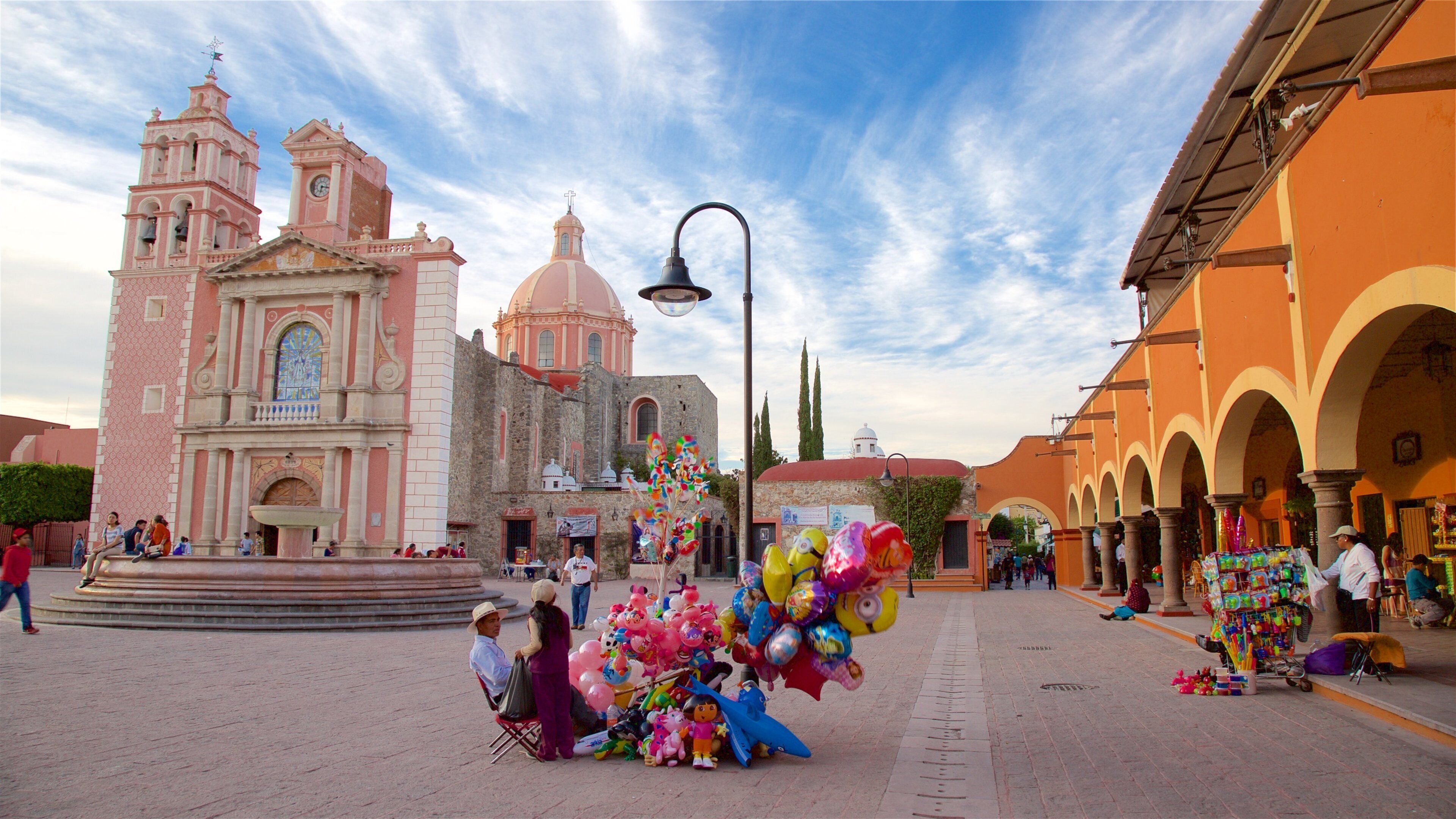 A plaza with a pink church, a fountain, and colorful balloons.