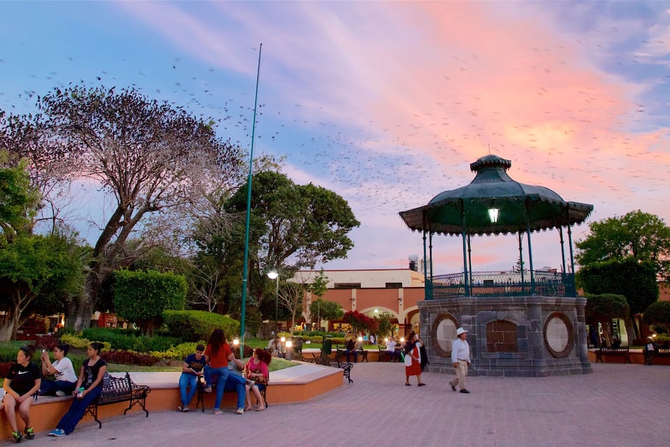 A park with a gazebo, benches, trees, and people.