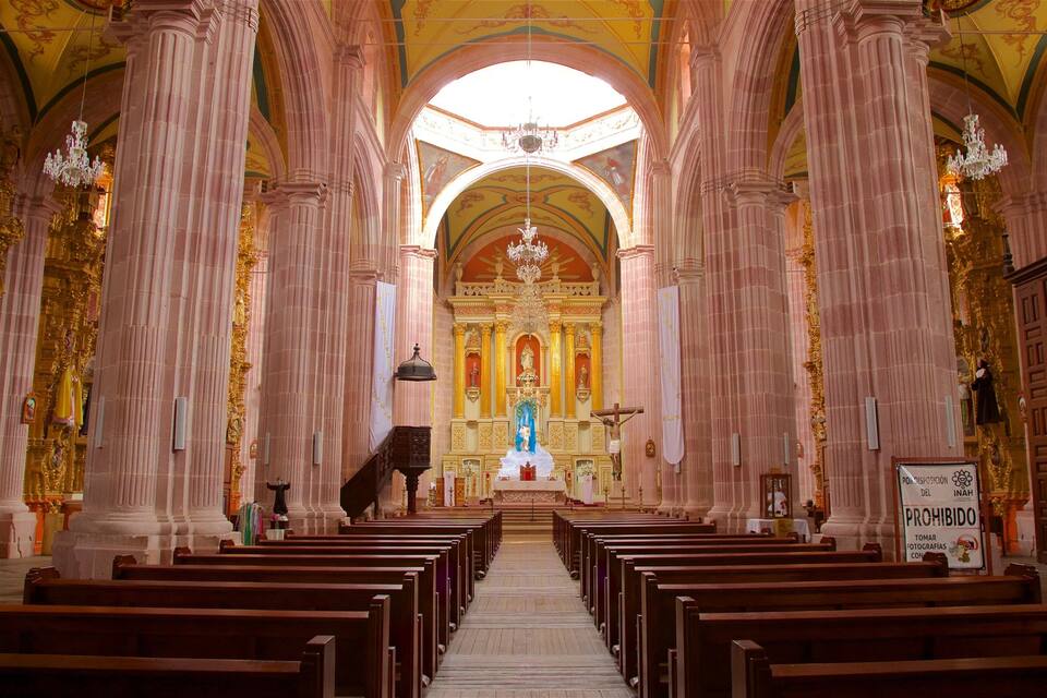 An ornate church interior with rows of pews, a central altar, and a chandelier.