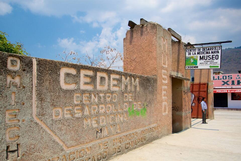 A weathered stone wall with inscriptions, a sign for 'Centro de Desarrollo de Medicina Maya', and a building with a red awning.