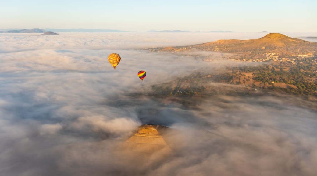 Hot air balloons rising above a dense cloud cover during sunrise, with the golden hues of the morning sun reflecting on the top of the Pyramid of the Sun at Teotihuacan, Mexico