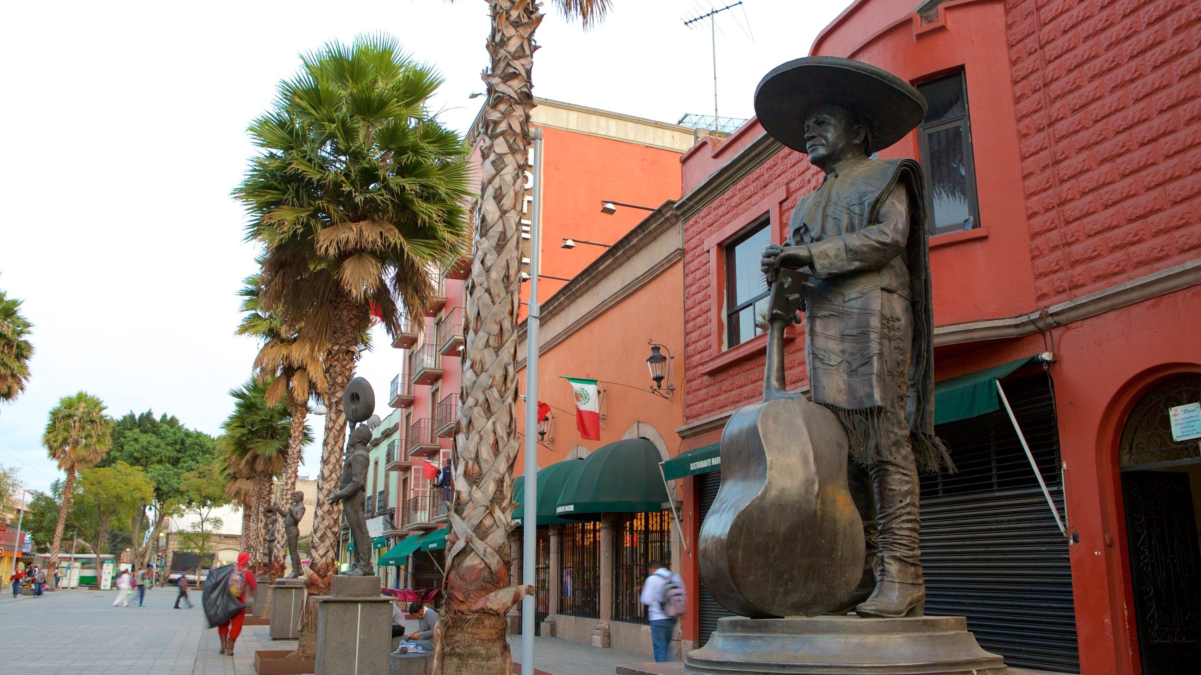 A street lined with palm trees and statues, with red buildings and a green awning.