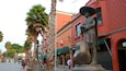 A street lined with palm trees and statues, with red buildings and a green awning.
