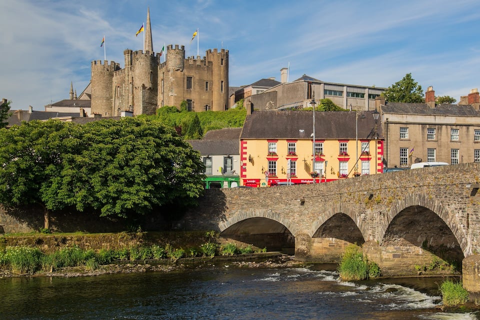 Un pont de pedra sobre un riu, un castell i un edifici colorit amb un rètol que diu "Lounge".