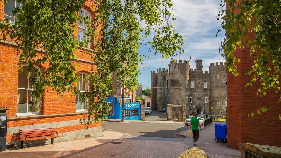 A cobblestone street with a red brick building, a blue sports shop, and a castle in the background.