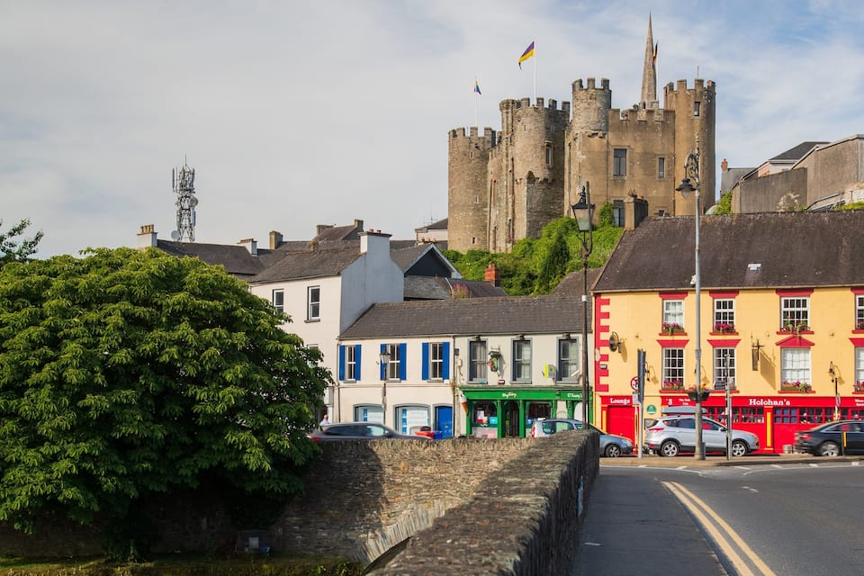 A street with colorful buildings, a castle in the background, and a stone wall.