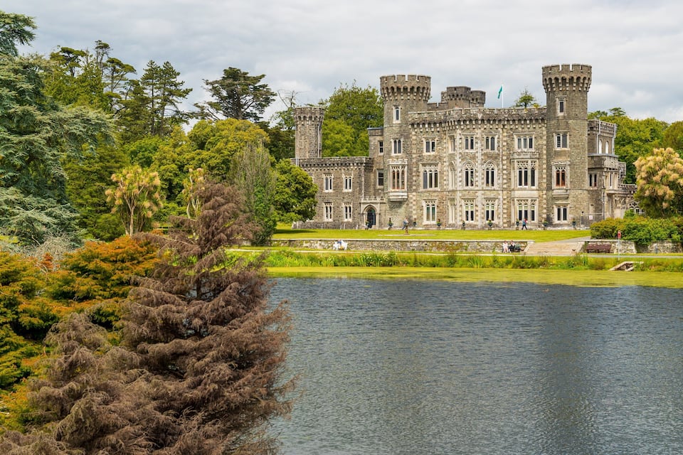 A large stone castle with multiple towers, surrounded by lush greenery and a lake.