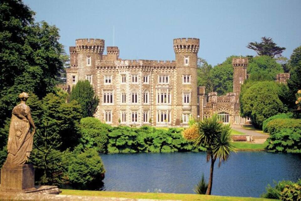 A castle with a moat, surrounded by lush greenery and a statue.