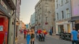 A busy street with shops, a stone building, and people walking.
