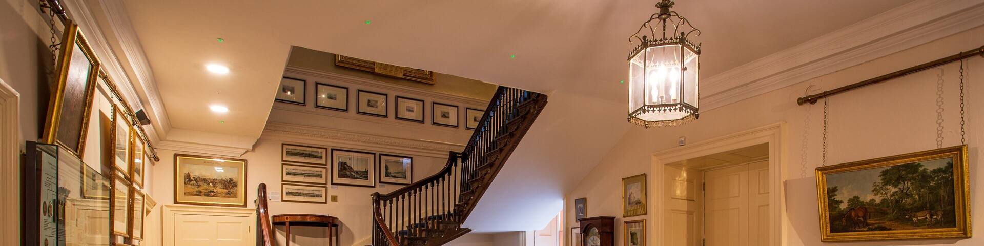 A grand staircase with blue carpet and wooden railings, a chandelier, and framed pictures on the walls.