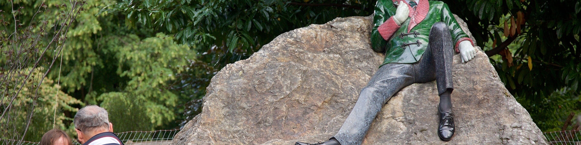Una estatua de un hombre con una chaqueta verde y corbata roja sentado sobre una roca grande.