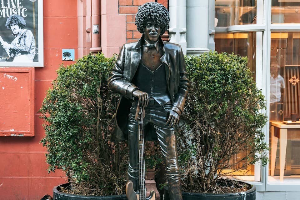 A statue of a man with a guitar, a red building, and a poster on the wall.