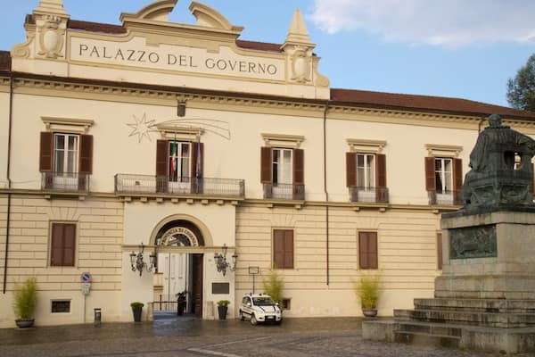 Ein historisches Gebäude namens „Palazzo Del Governo“ mit klassischer Architektur, einer Statue und einem geparkten Auto davor.