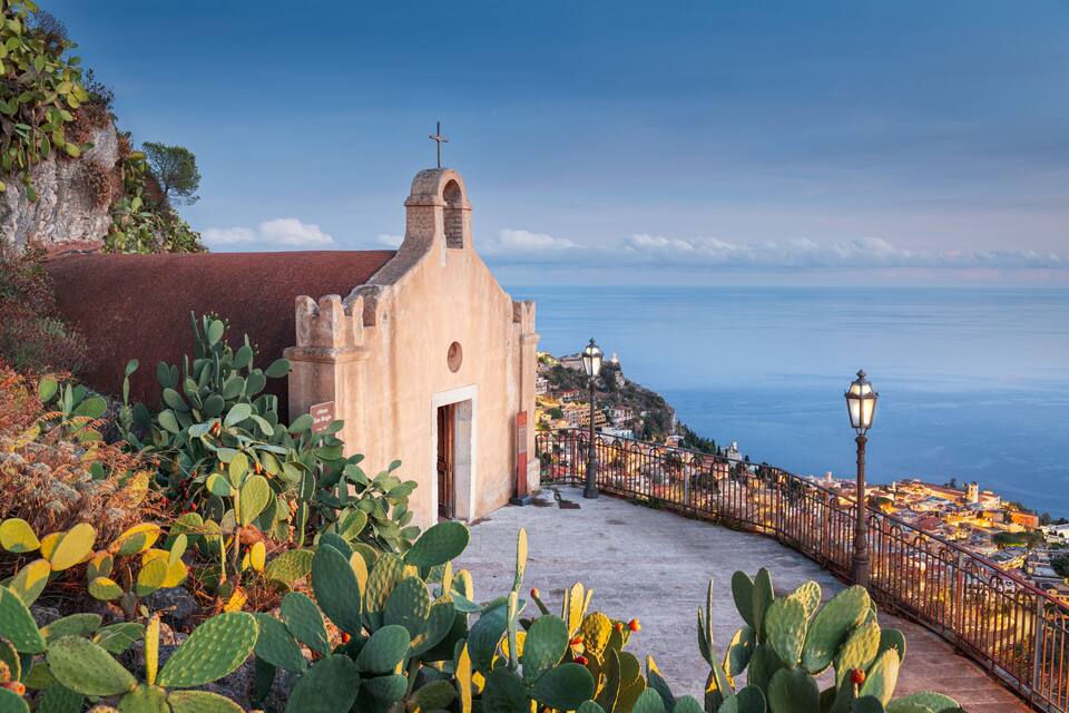 Una iglesia costera con una cruz en la parte superior, con vistas a un pueblo y al mar.