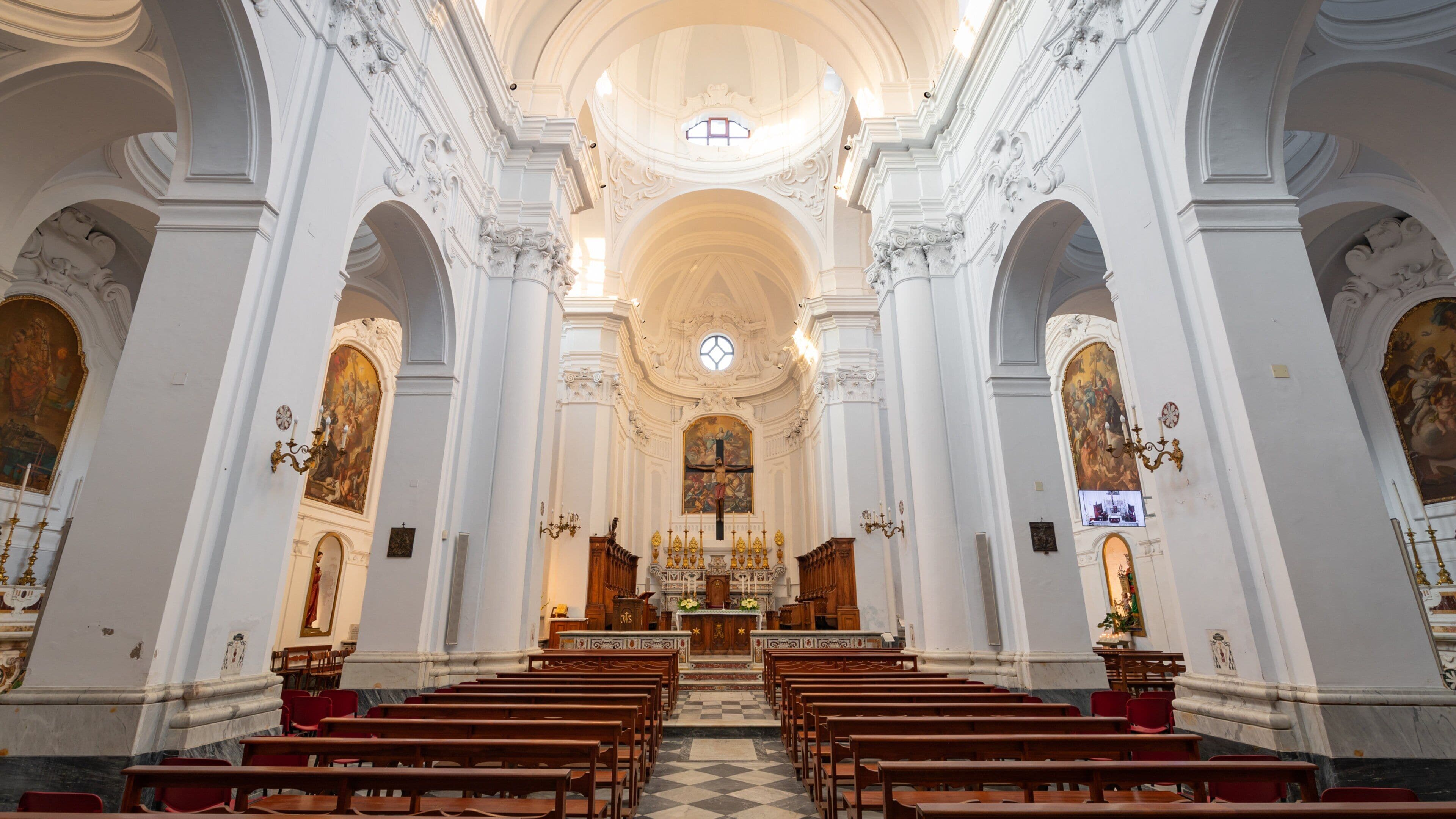 An ornate church interior with high ceilings, detailed frescoes, and rows of wooden pews.