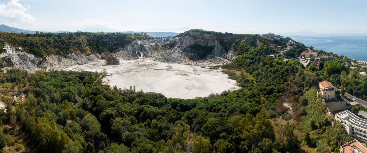 A volcanic crater surrounded by dense forest and coastal buildings.