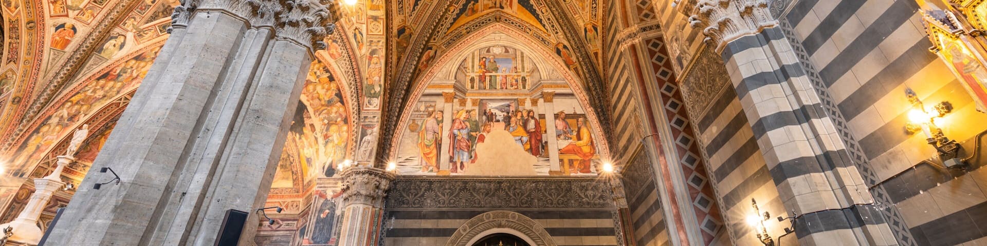 A cathedral's interior with intricate frescoes, pointed arches, and ornate columns.