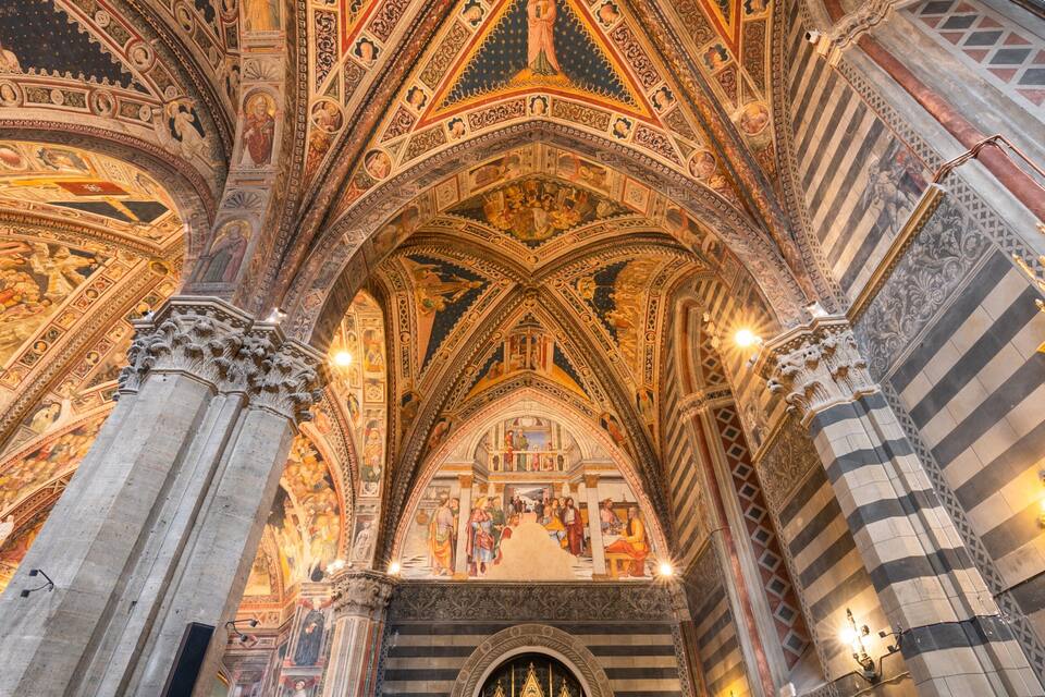 Interior de uma catedral com afrescos detalhados, arcos ogivais e colunas ricamente decoradas.
