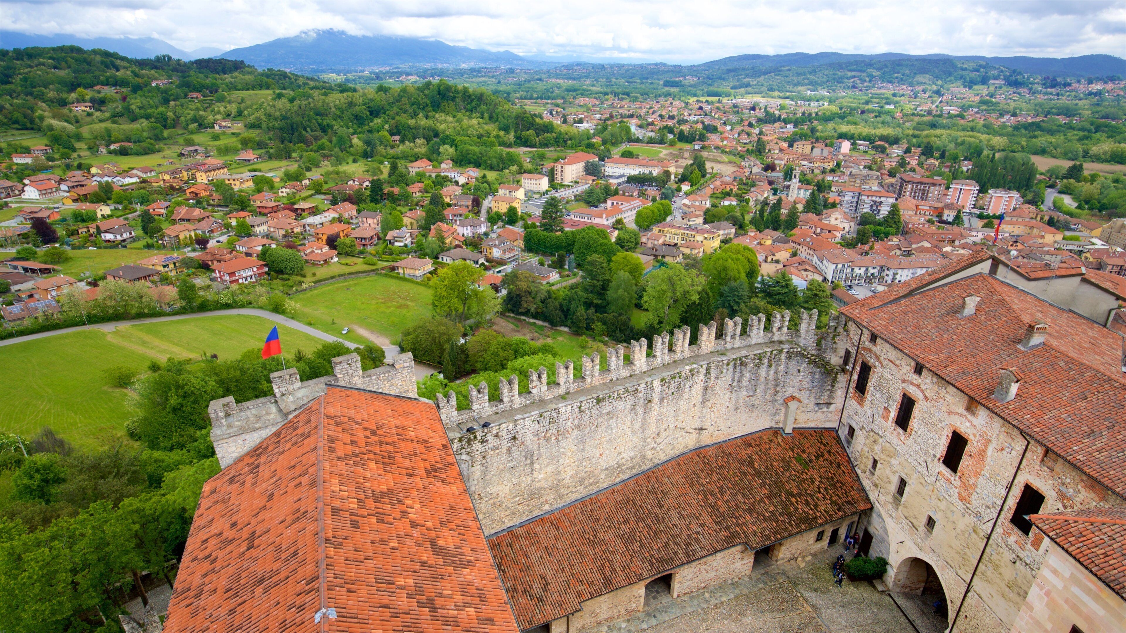 A historic town with a prominent castle, lush green hills, and a river in the background.